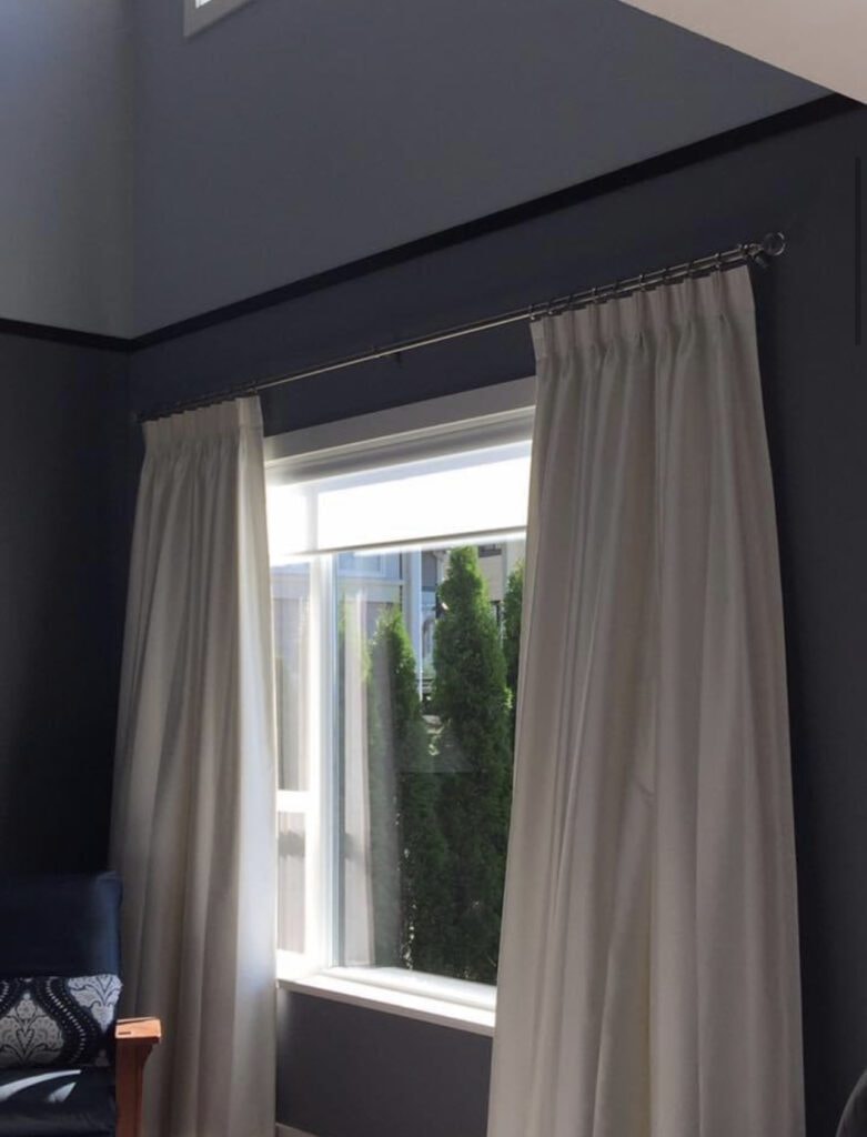 Cream pinch pleat curtains on dark wall with garden view