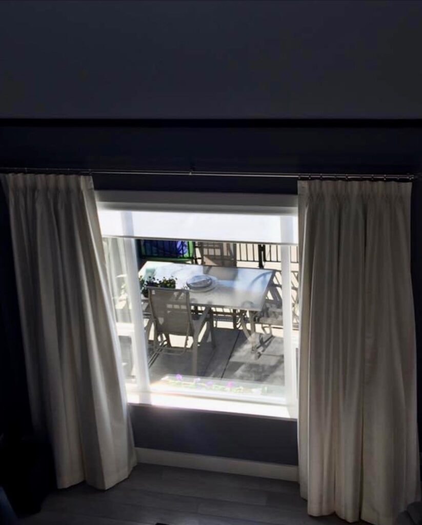 Cream pinch pleat drapes with roller blind on balcony window