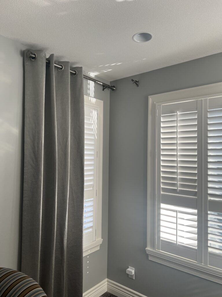 Grey grommet curtains with white plantation shutters in bedroom